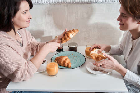 Lesbian couple enjoying breakfast while drinking juice and eating croissantsの写真素材