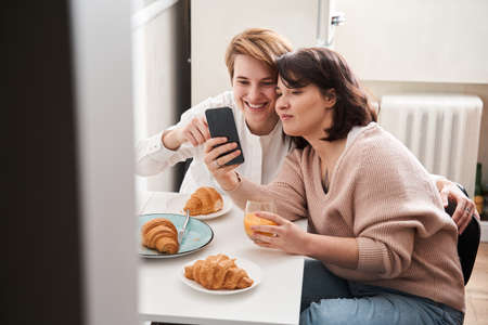 Girls making photo after eating croissants and drinking juice at the kitchenの写真素材