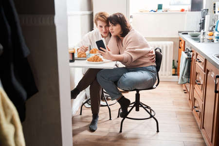 Woman holding smartphone while making photo with her happy girlfriendの写真素材