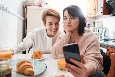 Lesbian couple holding smartphone and posing while making selfie togetherの写真素材