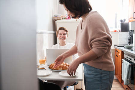 Girl cleaning the table after breakfast while chatting with her girlfriendの写真素材