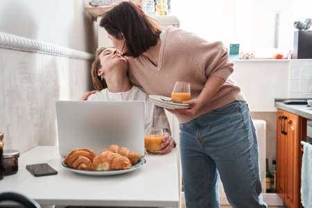 Girl kissing her lovely girlfriend while cleaning the table after breakfastの写真素材