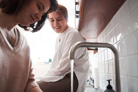 Woman looking at her girlfriend while she washing plates and smilingの写真素材