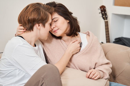 Lesbian couple relaxing on a couch at home while enjoying spending time togetherの写真素材