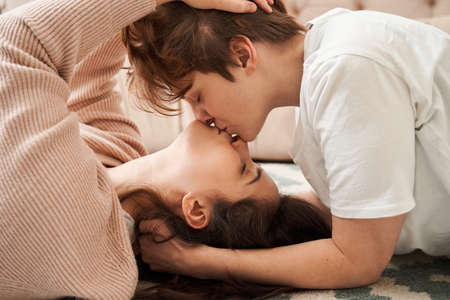 Woman kissing her girlfriend while laying together at the carpet at the floorの写真素材