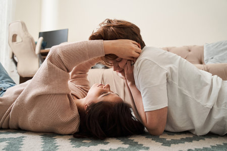 Lesbian couple looking at each other while laying together at the floorの写真素材