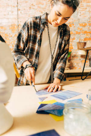 Female master wearing plaid shirt working on new modern colorful mosaic