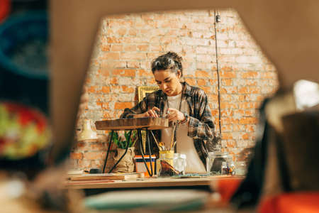 Girl in plaid shirt standing at her loft studio and making wonderful mosaicの写真素材