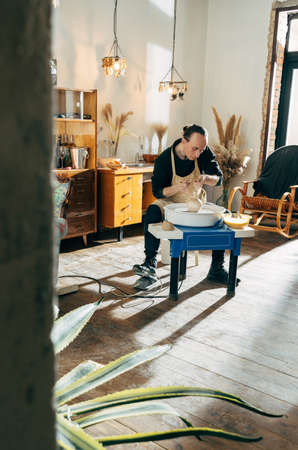 Full length view of the man sitting at his workshop and making vase