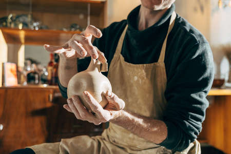 Satisfied adult pottery man holding at his hands finished pottery vase and showingの写真素材