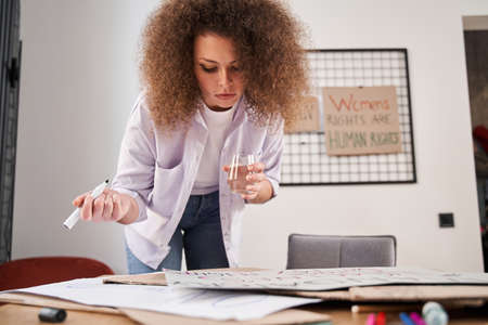 Curly female working with slogans while drawing it at the cupboard in workshop