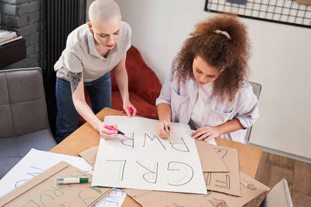 Girls drawing handmade poster about feminism at the table with each otherの写真素材