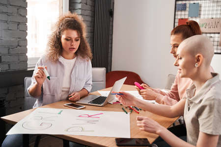 Girls chatting with each other while drawing handmade poster about feminism
