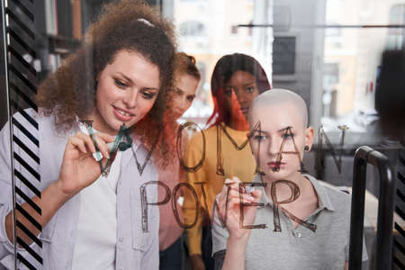 Girls writing slogans about womens rights at the transparent glass