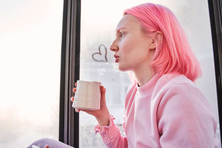 Woman with pink hair warming herself with hot beverage
