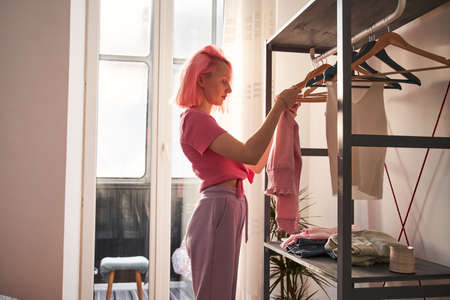 Woman with pink hair standing at the bedroom and choosing clothes