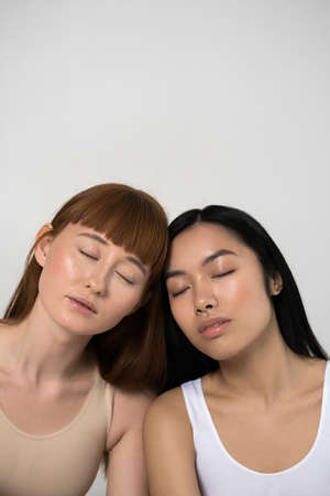 Women bonding to each other while posing with closed eyes on grey background