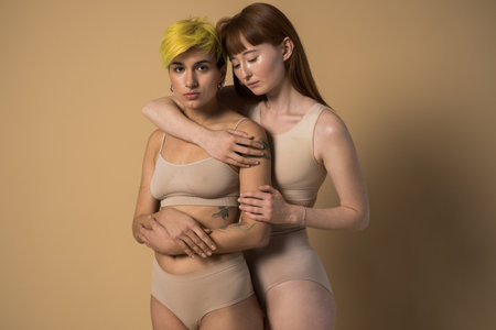 Ginger girl with long hair and tattooed girl with yellow hair embracingの写真素材