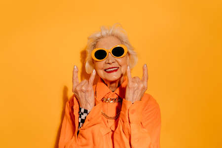 Woman standing over isolated yellow background while doing rock symbol