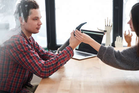 Man holding robotic hand while discussing it with his female client or colleague