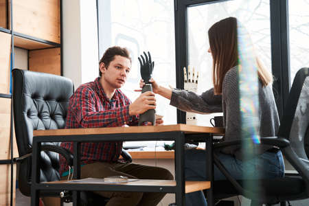 Man holding black artificial limb and telling something to his female colleague