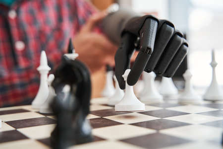 Engineer holding chess piece with black bionic hand while playing at the chessの写真素材