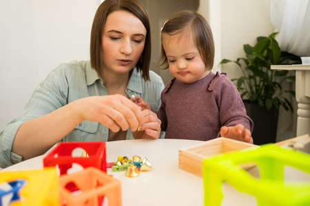 Girl with down syndrome playing with her toys at the table with her motherの写真素材