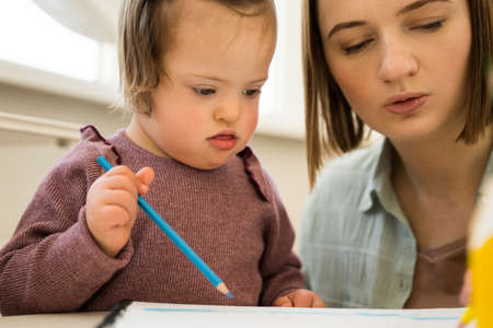 Girl with down syndrome drawing diligently near her mother