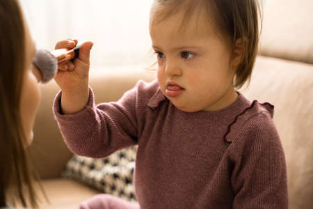 Down syndrome child making makeup for her mother while holding brushの写真素材