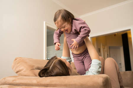 Mother laying at the sofa and playing with her daughter with down syndrome