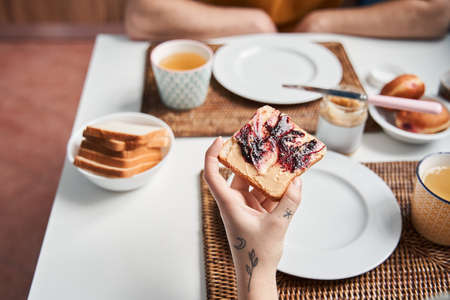 Woman holding a toast with peanut butter and jam while having breakfast