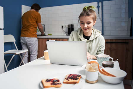 Man washing plates while his lovely girlfriend working at the laptop nearbyの写真素材