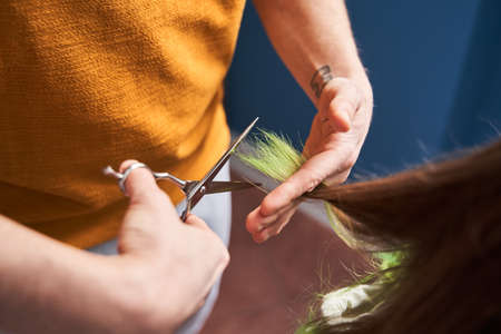 Man holding colored hair tips of his wife while cutting it at the kitchen