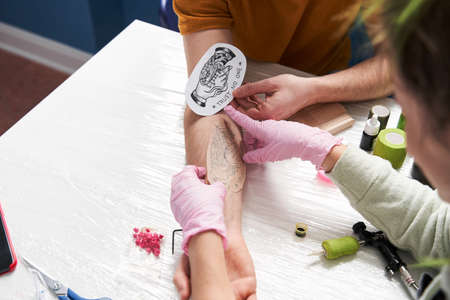 Woman wearing protective pink medical gloves choose a place for future tattoo