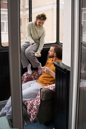 Woman sitting at the windowsill at the balcony and showing something to her man