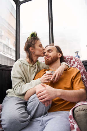 Woman kissing her beloved man while drinking coffee together