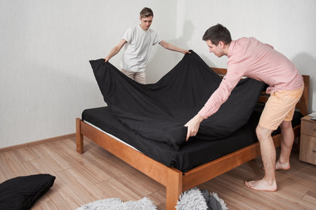 Homosexual couple making their bed early in the morning while looking happy