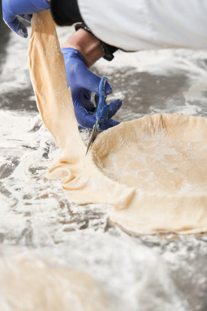 Baker hands cut the dough with scissors while preparing pie at the table