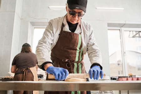 Baker man kneading dough on table with flour and rolling pin