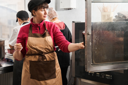Baker standing at the industrial kitchen and putting cake or pie at the oven