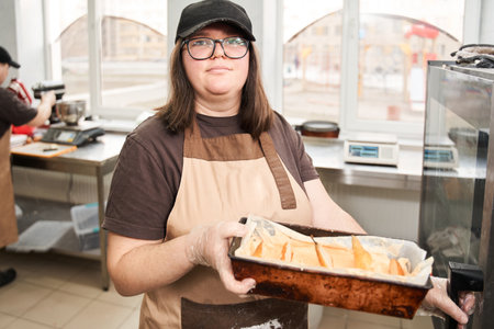Female baker wearing apron standing at the industrial kitchen and holding cake