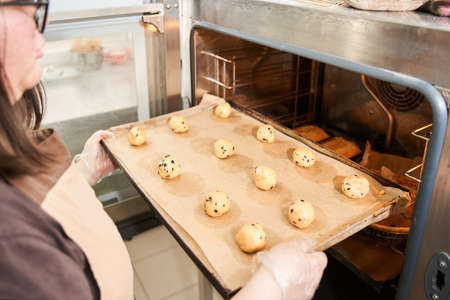 Baker putting tray with balls from the dough to the oven