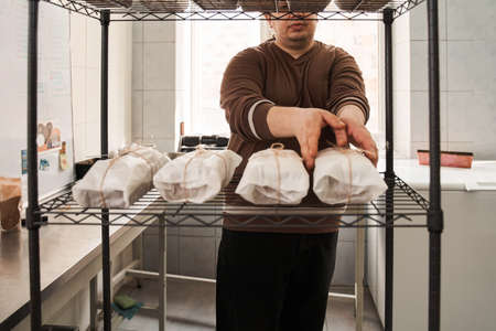 Male worker putting packing cakes on a bakery trolley