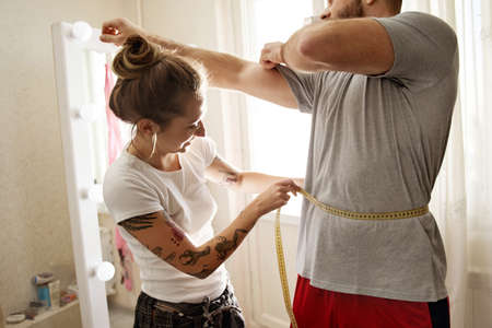 Woman measuring her boyfriend with centimeter type while controlling parametersの写真素材
