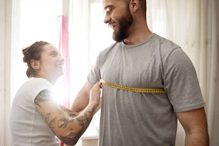 Woman measuring her boyfriend with centimeter type while controlling parametersの写真素材