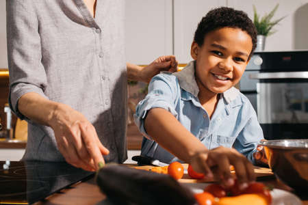 Boy stretching for the pepper while helping to his mother preparing foodの写真素材