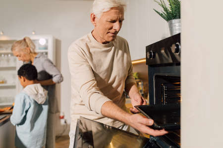 Man opening the oven while preparing to the baking dish for the dinnerの写真素材