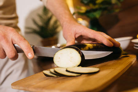 Man chopping eggplant on wooden chopping board in modern kitchenの写真素材