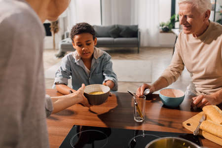 Woman giving plate with soup to the multiracial boy while having dinnerの写真素材