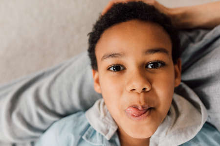 Boy resting at knees of his caucasian mother and showing tongue to the cameraの写真素材